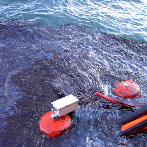 Oil spill in the ocean with containment equipment and floating barriers.