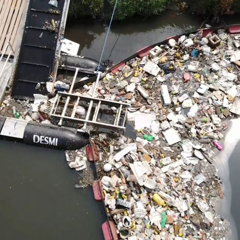 DESMI waste collection system intercepting floating debris in a river.