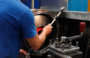Technician measuring machine part with a gauge in an industrial setting.