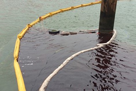Oil spill containment with yellow boom and absorbent materials near a pier.