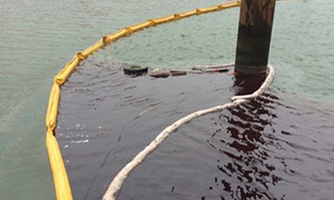 Oil spill containment with yellow boom and absorbent materials near a pier.