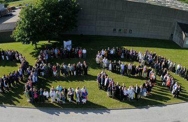 Aerial view of people forming the word "DESMI" on a grassy area.