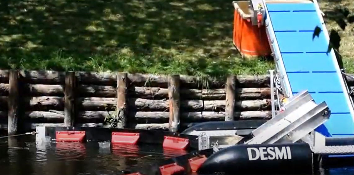DESMI oil spill recovery system with conveyor belt operating by a riverside.
