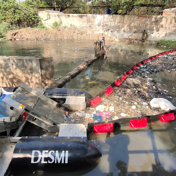 DESMI system collecting debris from a polluted river using a floating barrier.