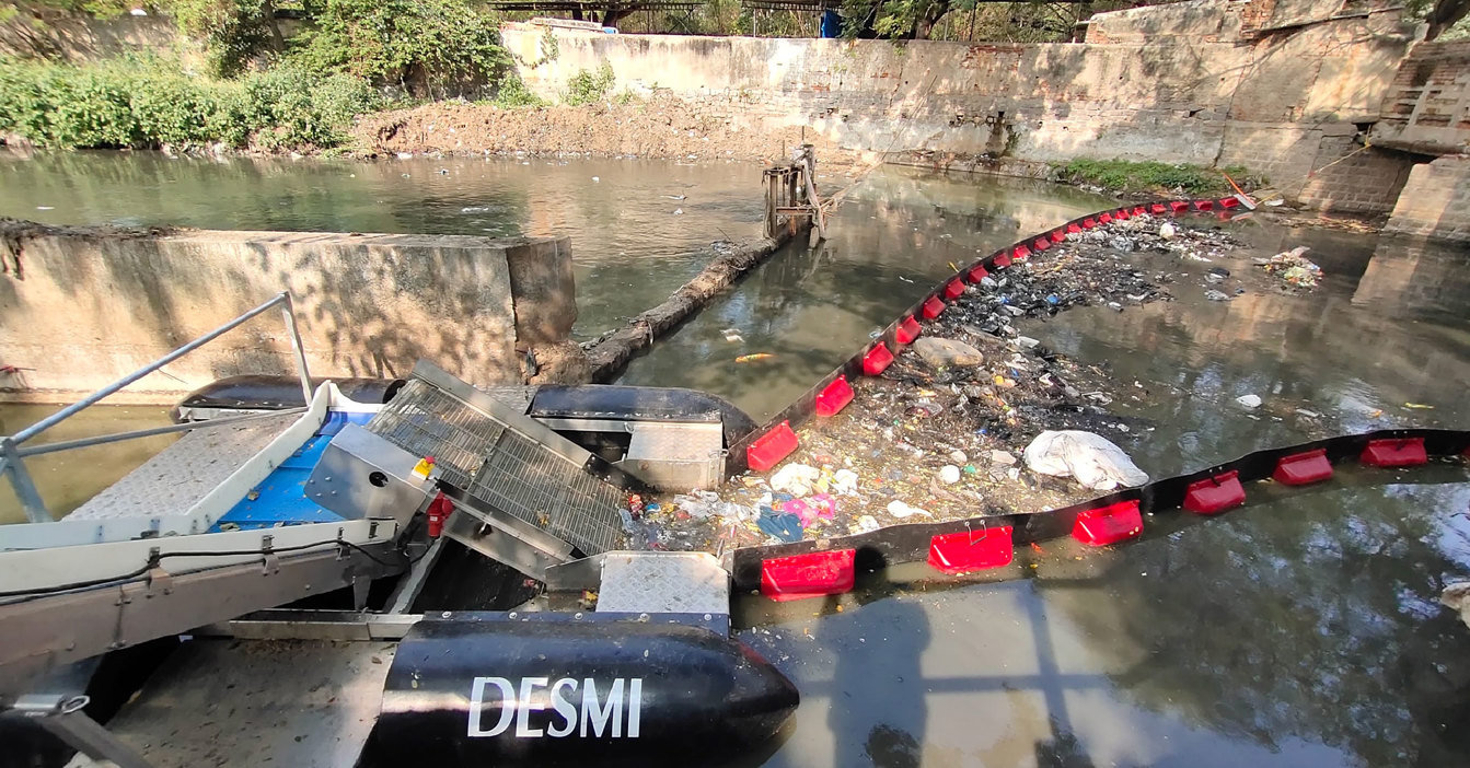 DESMI system collecting debris from a polluted river using a floating barrier.