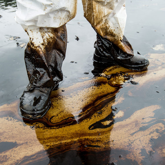 Person in protective gear standing in oil-contaminated water.