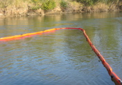 Orange floating barrier on a river, used for oil spill containment.