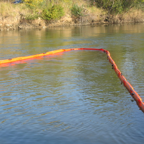 Orange floating barrier on a river, used for oil spill containment.