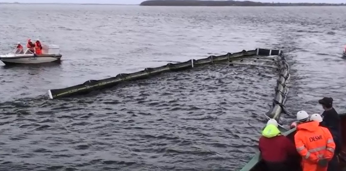 People deploying DESMI oil containment boom in the water from a boat.
