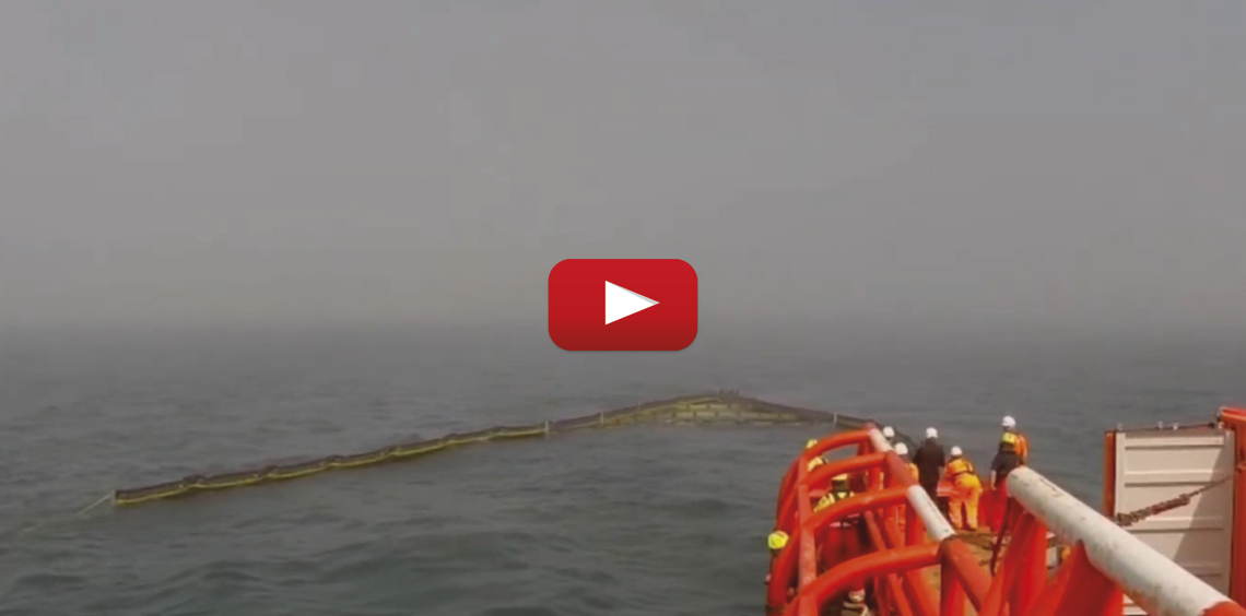 Workers deploying an oil containment boom at sea from a vessel.