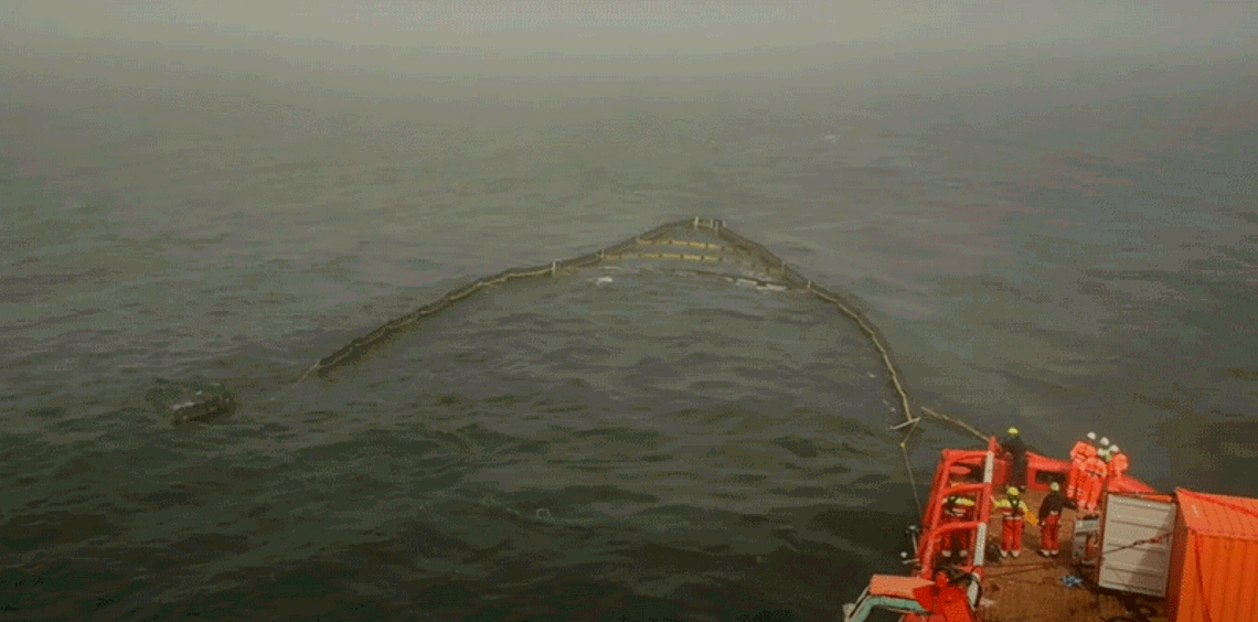 Workers on a vessel deploying an oil spill containment boom at sea.