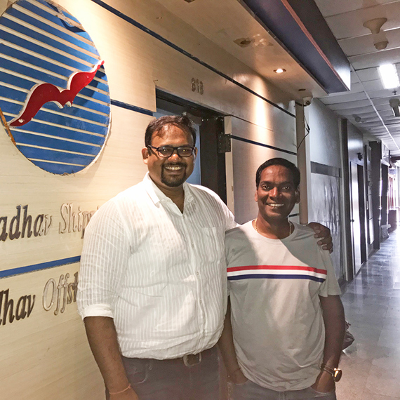 Two people smiling in front of Sadhav Shipping office sign.