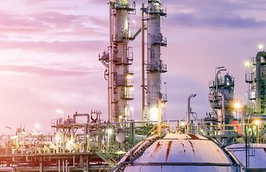 Industrial refinery complex illuminated against a colorful sunset sky.