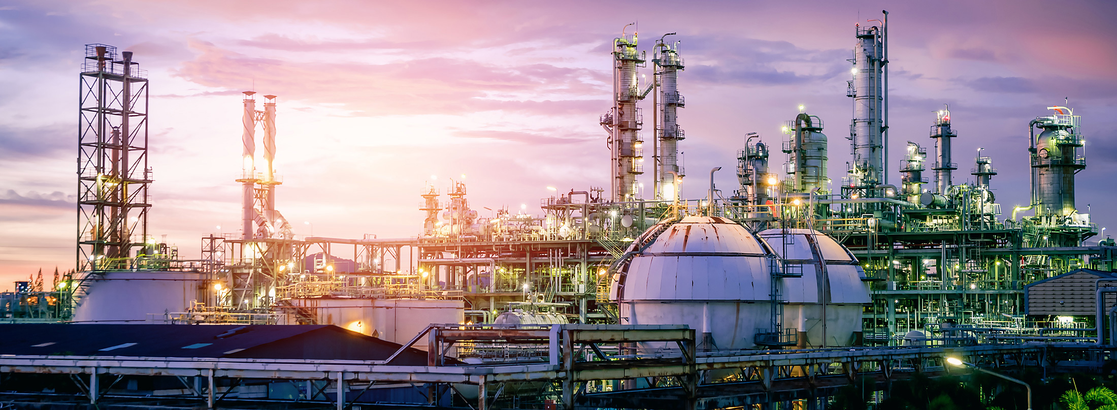 Industrial refinery complex illuminated against a colorful sunset sky.