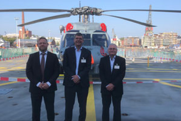 Three men in suits standing in front of a helicopter on a helipad.