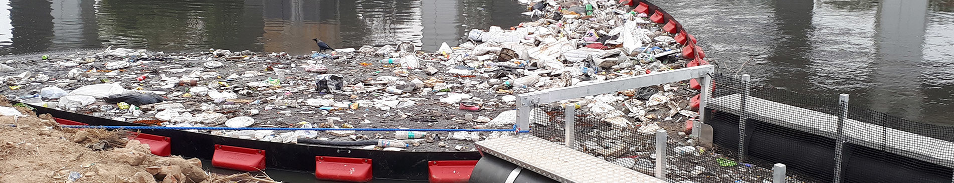 River with floating trash barrier filled with debris and garbage.
