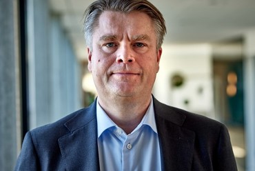 Man in a suit standing in a well-lit hallway.