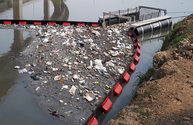 DESMI barrier containing floating debris on a polluted river surface.