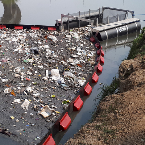 DESMI barrier containing floating debris on a polluted river surface.