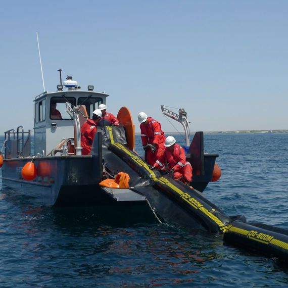 Workers deploy oil containment boom from a boat on open water.