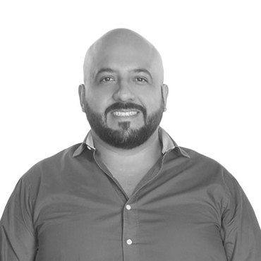 Smiling man with a beard wearing a button-up shirt in a black-and-white photo.