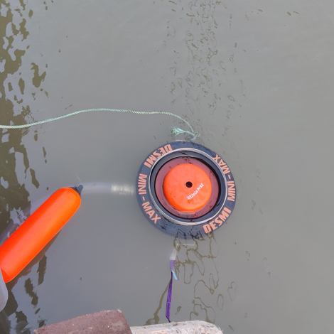 DESMI Mini-Max skimmer floating in water, attached to a hose for fluid handling.