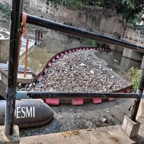 DESMI trash rake removing debris from a waterway near a concrete embankment.