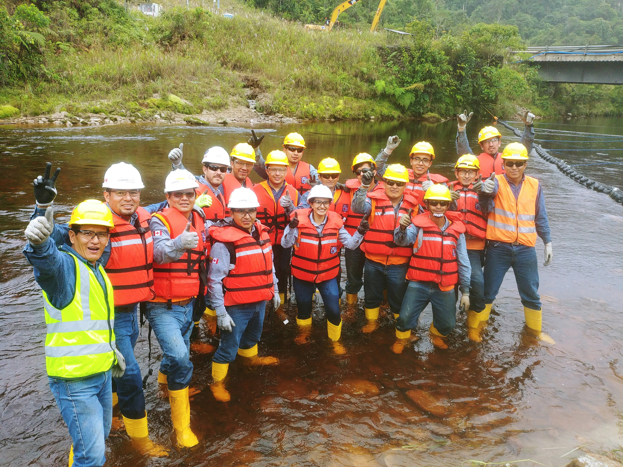 Group of workers in protective gear standing in a river, posing cheerfully.