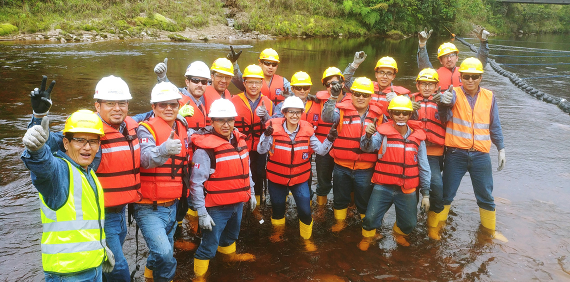 Group of workers in protective gear standing in a river, posing cheerfully.