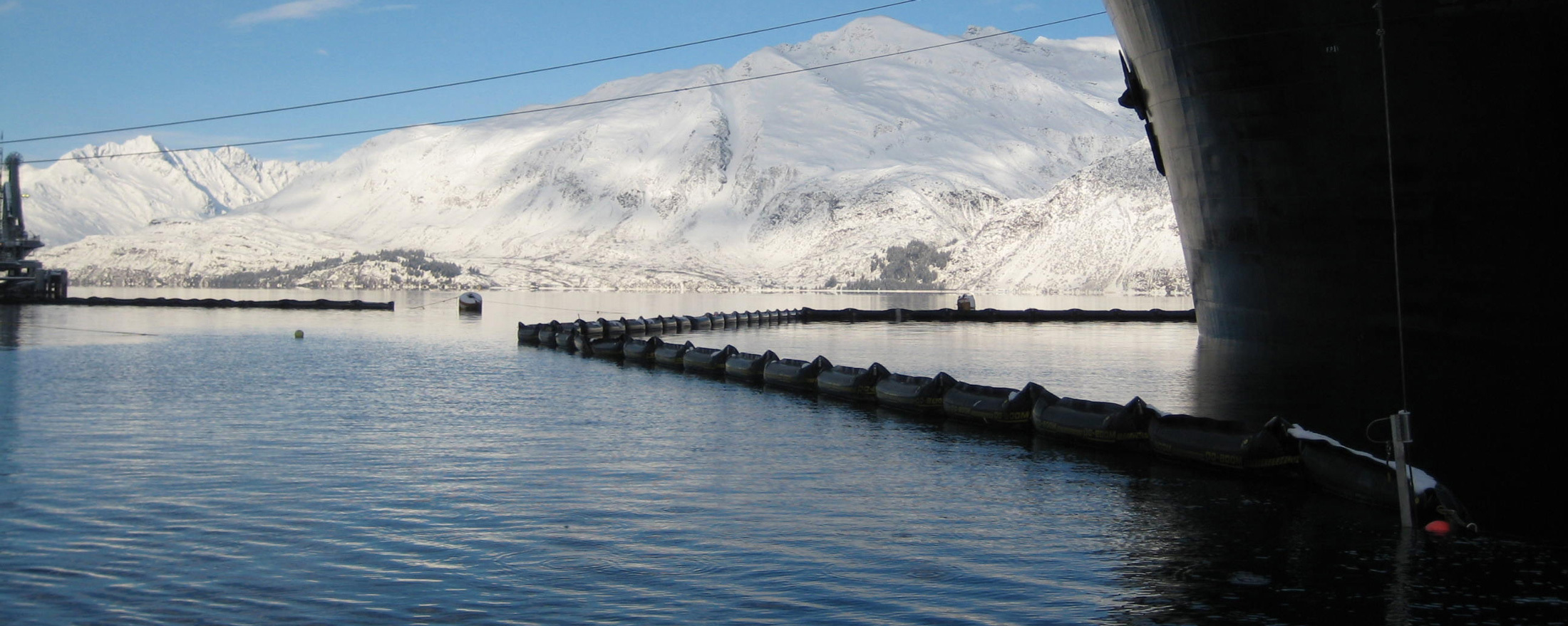 Oil spill containment boom on water with snowy mountains in the background.