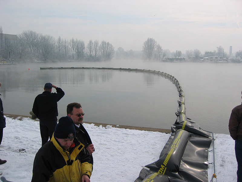 People observing a floating barrier on a misty lake in winter.