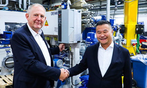 Two men shaking hands in front of DESMI equipment in an industrial setting.