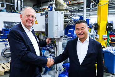Two men shaking hands in front of DESMI equipment in an industrial setting.