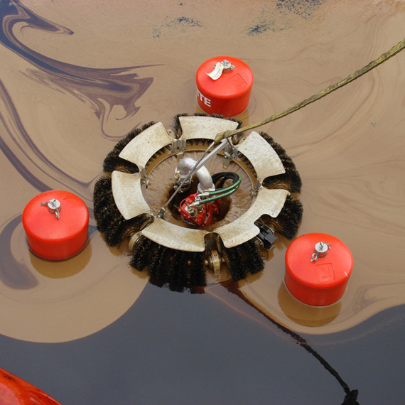 Oil skimmer device floating in water, surrounded by red buoys.