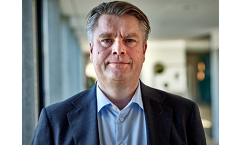 Man in a suit standing in a well-lit hallway.