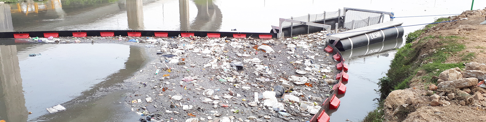 DESMI trash barrier in river, collecting floating debris and waste efficiently.